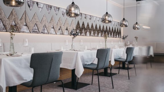 An elegant restaurant with modern tables and chairs. The walls are decorated and stylish lamps hang from the ceiling. - The Crystal VAYA Unique - Obergurgl 