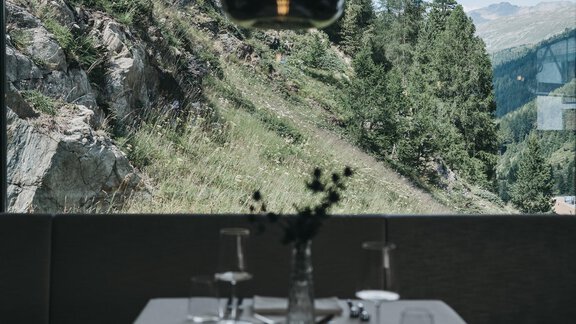 An elegant table in a restaurant with a view of a green mountain landscape. A modern lamp hangs above the table. - The Crystal VAYA Unique - Obergurgl 