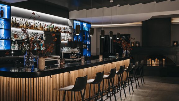 A stylish bar with an elegant wooden counter and blue light accents. In the background, various spirits and a cozy atmosphere can be seen. - The Crystal VAYA Unique - Obergurgl 