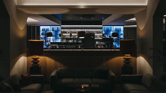A stylish bar with soft lighting and modern furniture. In the background, several shelves with drinks are illuminated. - The Crystal VAYA Unique - Obergurgl 