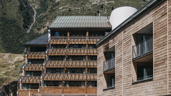 A modern hotel building set in a mountainous landscape. The architecture combines wood and concrete and offers balconies with views of nature. - The Crystal VAYA Unique - Obergurgl 