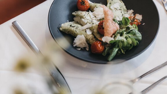 A plate with fresh salad, gnocchi, and cherry tomatoes on an elegant table. In the foreground, there is a glass of white wine and a small flower decoration. - The Crystal VAYA Unique - Obergurgl 