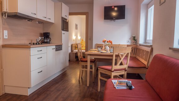 A cozy apartment with a modern kitchen and a dining area. In the corner, there is a red sofa and a television is mounted on the wall. - Alpenapart Saphir - Sölden