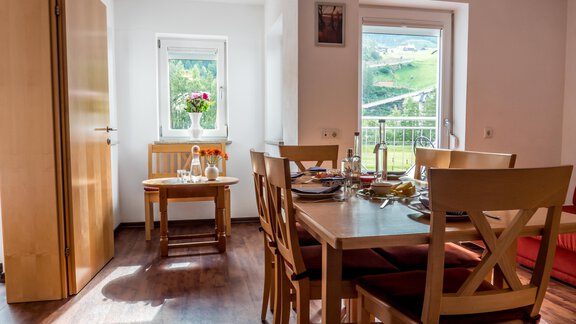 A bright and inviting dining room with a table and chairs. Through the window, you can see a green landscape and blooming plants. - Alpenapart Saphir - Sölden