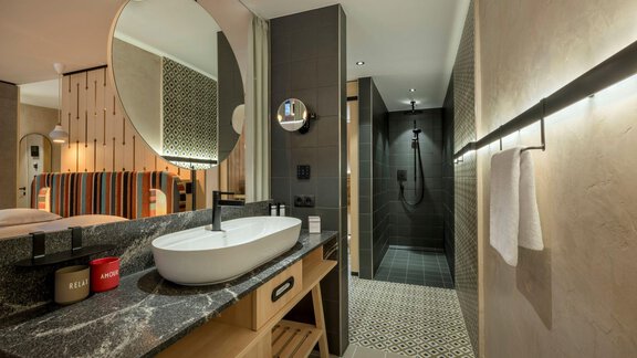 A modern bathroom with an elegant sink console and a large shower. The decor is stylish and well-lit, with beautiful tiles. - Alpengasthof Grüner - Sölden