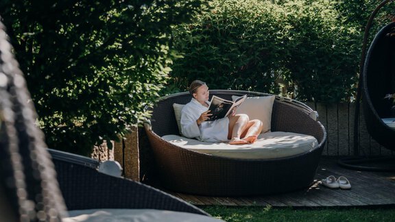 A person sits comfortably in a round lounge chair and reads a book. The surroundings are green and peaceful, ideal for relaxing. - Alpengasthof Grüner - Sölden