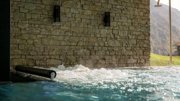 A modern pool with crystal clear water and a stone wall in the background. Gentle water waves create a relaxing atmosphere. - Alpengasthof Grüner - Sölden
