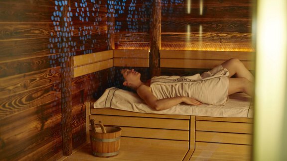 A person is relaxing in a sauna on a wooden bench. The atmosphere is warm and soothing. - Alpengasthof Grüner - Sölden