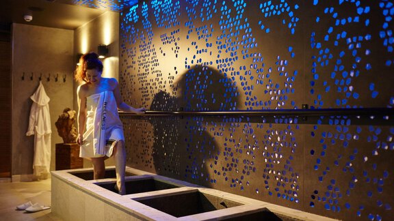 A modern wellness facility with stylish accents. A woman carefully enters a water basin under soft blue light. - Alpengasthof Grüner - Sölden