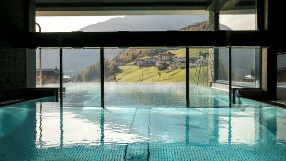 An elegant swimming pool with views of green hills and mountains. The water's surface reflects the tranquil atmosphere. - Alpengasthof Grüner - Sölden