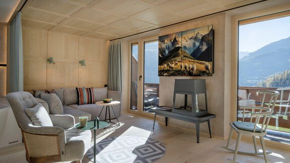 A modern living room with a comfortable sofa and a table. Large windows offer a view of the mountains and provide plenty of daylight. - Alpengasthof Grüner - Sölden