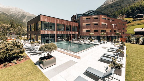 Ein modernes Hotel mit einem Pool und Liegen im Freien. Umgeben von grünen Wiesen und Bergen bietet es eine entspannende Atmosphäre. - AlpenParks The Secret Sölden - Sölden