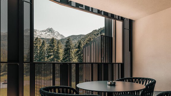 Ein modernes Balkon mit einem runden Tisch und Stühlen. Im Hintergrund sieht man beeindruckende Berge und Wälder. - AlpenParks The Secret Sölden - Sölden