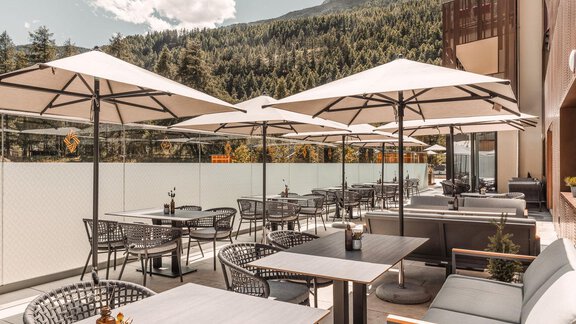 Eine moderne Terrasse mit Sitzplätzen und Sonnenschirmen. Im Hintergrund sind Bäume und Berge zu sehen. - AlpenParks The Secret Sölden - Sölden