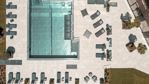 Ein modern gestalteter Poolbereich mit Liegen und Sonnenschirmen. Die Umgebung ist mit Grünflächen und Pflanzen dekoriert. - AlpenParks The Secret Sölden - Sölden