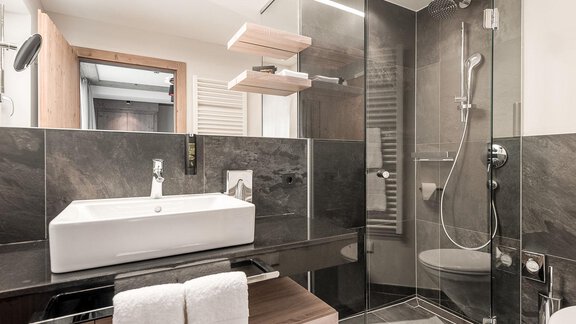 Ein modernes Badezimmer mit eleganten Fliesen und einer Glasdusche. Die Einrichtung umfasst ein stilvolles Waschbecken und Holzdetails. - AlpenParks The Secret Sölden - Sölden