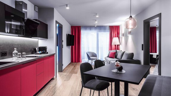 Eine moderne Wohnung mit roter Küchenschrankfront und stilvollen Möbeln. Der Raum ist hell und offen mit großen Fenstern und einem gemütlichen Essbereich. - AlpenParks The Secret Sölden - Sölden