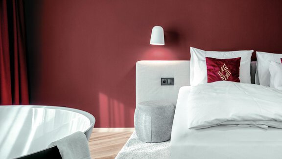 Ein modernes Schlafzimmer mit rot gestrichenen Wänden. Das Zimmer ist stilvoll eingerichtet mit einem gemütlichen Bett und einer freistehenden Badewanne. - AlpenParks The Secret Sölden - Sölden