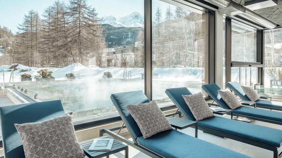 Ein gemütlicher Wellnessbereich mit Liegen und Blick auf einen Schwimmteich in einer winterlichen Landschaft. Draußen sind schneebedeckte Bäume und Berge zu sehen. - AlpenParks The Secret Sölden - Sölden