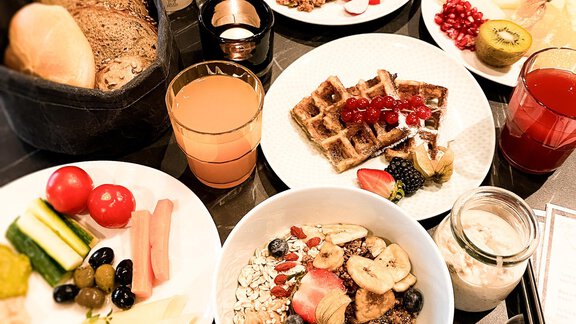 Ein reichhaltiges Frühstücksbuffet mit verschiedenen Speisen, einschließlich Obst, Waffeln, Joghurt und Brot. Frische Säfte und eine Auswahl an Beilagen runden das Angebot ab. - AlpenParks The Secret Sölden - Sölden