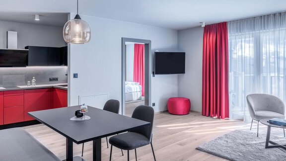 Das Bild zeigt ein modernes Zimmer mit einer Kitchenette und einem Esstisch. Die Einrichtung ist stilvoll mit roten Vorhängen und einer gemütlichen Sitzecke. - AlpenParks The Secret Sölden - Sölden
