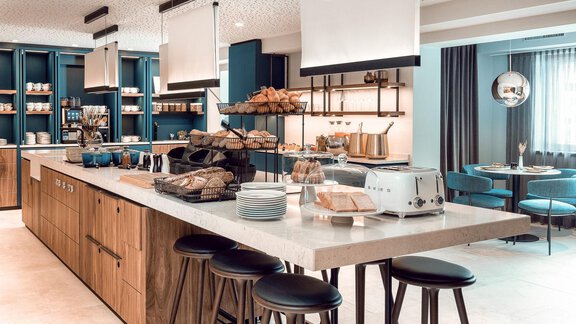 Eine moderne Küche mit einem langen Esstisch und Stühlen. Auf der Theke befinden sich verschiedene Lebensmittel wie Brötchen und ein Toaster. - AlpenParks The Secret Sölden - Sölden