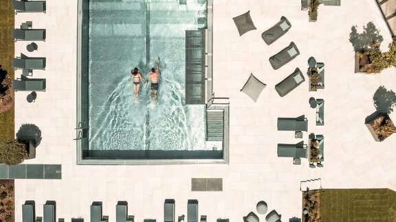 Ein modernes Schwimmbad mit zwei Personen, die im Wasser schwimmen. Rund um das Becken liegen elegante Liegen und Sitzgelegenheiten auf einer gepflegten Terrasse. - AlpenParks The Secret Sölden - Sölden