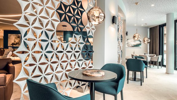 Ein modernes Café mit stilvollen, blauen Stühlen und eleganten Lampen. Eine dekorative Wand aus geometrischem Muster ergänzt die ansprechende Atmosphäre. - AlpenParks The Secret Sölden - Sölden