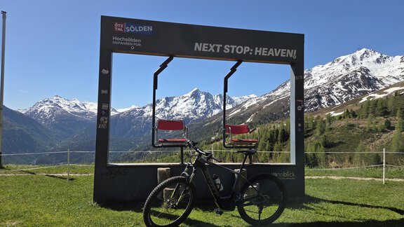 Ein schöner Aussichtspunkt mit einem Rahmen und zwei roten Stühlen vor majestätischen Bergen. Ein E-Bike steht im Vordergrund auf einer grünen Wiese. - Apart Alpenjuwel - Sölden