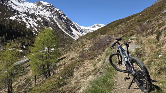 A mountain bike stands on a narrow path in the mountains. In the background, snow-covered peaks and a blue sky can be seen. - Apart Alpenjuwel - Sölden