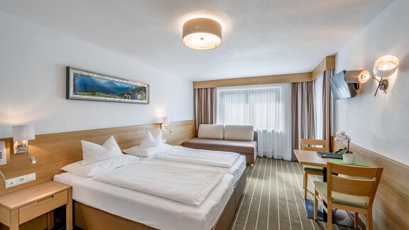 A modern hotel room with two single beds and a sofa bed. There is a large window area with natural light and simple wood decor. - Apart Hotel Garni Wieser - Sölden