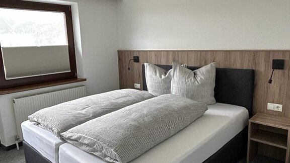 A modern bedroom with a double bed and large pillows. The room has a large window and a simple, pleasant decor. - Apart Romed - Sölden