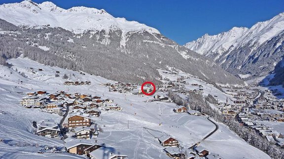 A picturesque winter landscape with snow-covered mountains and small houses. The clear blue sky creates a peaceful atmosphere. - Apart Romed - Sölden