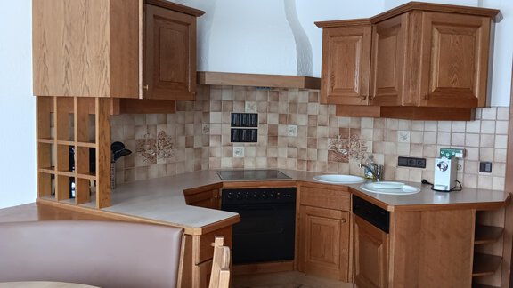 Eine moderne Küche aus Holz mit einer L-förmigen Anordnung. Sie verfügt über einen Herd, eine Spüle und ansprechende Fliesen. - Apart Romed - Sölden