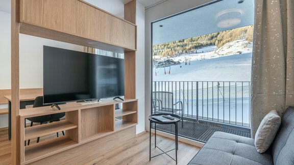 Ein modernes Wohnzimmer mit einem großen Fernseher und einem komfortablen Sofa. Durch die Fenster ist eine schöne Winterlandschaft mit Schnee zu sehen. - Apart Sonnenbichl - Sölden