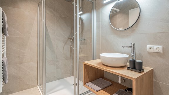 Ein modernes Badezimmer mit einer klaren Duschkabine und einem eleganten Waschbecken. Der Holzschrank bietet Platz für Handtücher und Pflegeprodukte. - Apart Sonnenbichl - Sölden