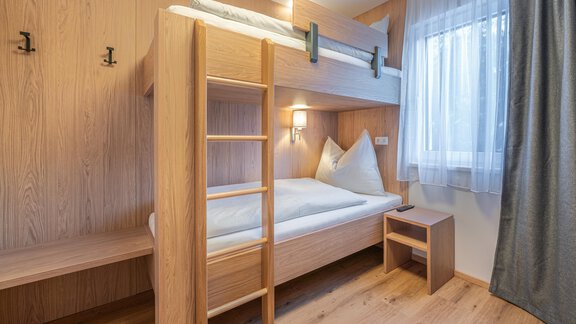 Ein modernes Zimmer mit einem Etagenbett aus Holz und einem kleinen Nachttisch. Die Fenster lassen viel Licht herein und die Wände sind hell gestaltet. - Apart Sonnenbichl - Sölden