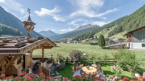 Eine malerische Landschaft mit grünen Wiesen und Bergen im Hintergrund. Im Vordergrund blühen bunte Blumen und ein Holzhaus ergänzt die idyllische Szenerie. - Apart Wiesengrund - Sölden