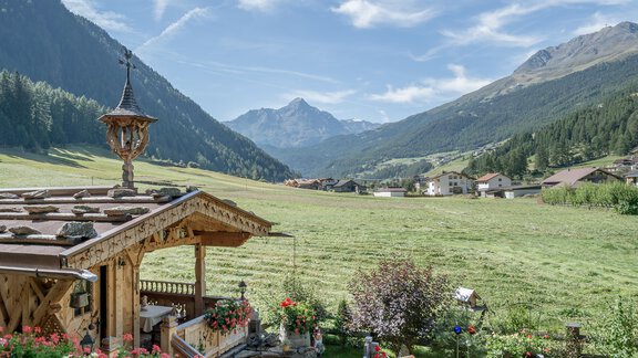 Eine malerische Berglandschaft mit einem Holzhaus und blühenden Blumen. Im Hintergrund sind majestätische Berge und ein blauer Himmel zu sehen. - Apart Wiesengrund - Sölden