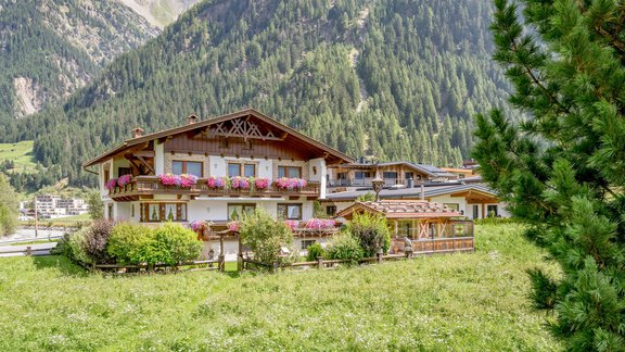 Ein malerisches Chalet umgeben von grünen Wiesen und majestätischen Bergen. Bunte Blumen schmücken die Fenster, was eine gemütliche Atmosphäre schafft. - Apart Wiesengrund - Sölden