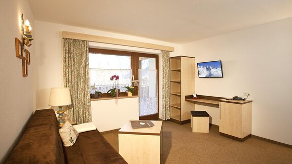 Ein gemütliches Wohnraum mit einem Sofa, einem Tisch und einem Fernseher. Große Fenster lassen viel Licht herein und bieten einen Blick nach draußen. - Appartement Alpin - Sölden