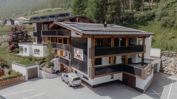 Ein modernes Gebäude in einer gebirgigen Umgebung, umgeben von Bäumen. Es gibt Parkplatzmöglichkeiten und einen einladenden Eingangsbereich. - Appartement Alpin - Sölden