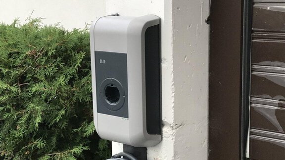 Eine Ladestation für Elektroautos, die an einer Wand installiert ist. In der Nähe sind grüne Pflanzen sichtbar. - Appartement Alpin - Sölden