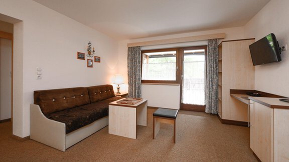 Ein gemütliches Wohnzimmer mit einem Sofa, einem Tisch und einem Fernseher. Große Fenster lassen viel Licht herein. - Appartement Alpin - Sölden