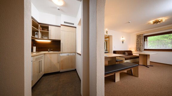 Eine moderne Küche mit Holzschränken und viel Platz. Der angrenzende Wohnbereich ist gemütlich eingerichtet und verfügt über große Fenster. - Appartement Alpin - Sölden