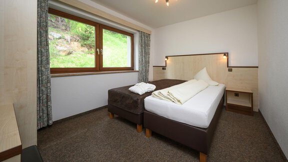 Ein einfaches Hotelzimmer mit zwei Betten und einem Fenster, das auf eine grüne Landschaft blickt. Die Wände sind hell und es gibt einen kleinen Tisch im Raum. - Appartement Alpin - Sölden