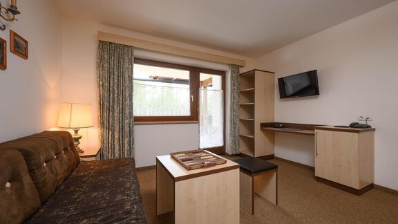 Ein gemütliches Wohnzimmer mit einem Sofa, einem Tisch und einem Fernseher. Der Raum hat große Fenster, die Tageslicht hereinlassen. - Appartement Alpin - Sölden