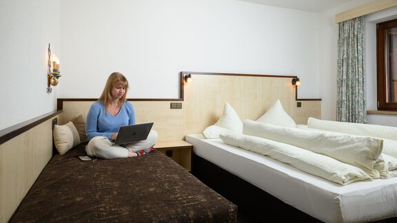Ein gemütliches Zimmer mit einem Bett und einem Sofa. Eine Person sitzt am Computer und arbeitet. - Appartement Alpin - Sölden