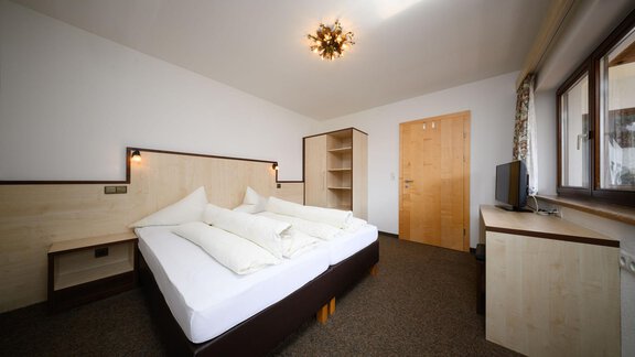 Ein modernes Schlafzimmer mit einem Doppelbett und hellen Holzmöbeln. Neben dem Bett stehen ein Schrank und ein Fernseher, und das Zimmer hat Fenster, die viel Tageslicht hereinzulassen. - Appartement Alpin - Sölden