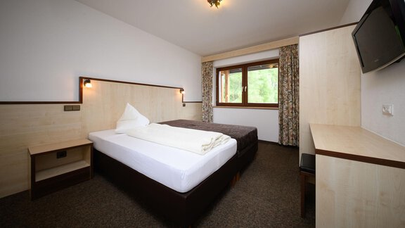 Ein einfaches Schlafzimmer mit zwei Betten und einem Fenster, das Blick auf die Natur bietet. Die Einrichtung ist modern und minimalistisch gehalten. - Appartement Alpin - Sölden
